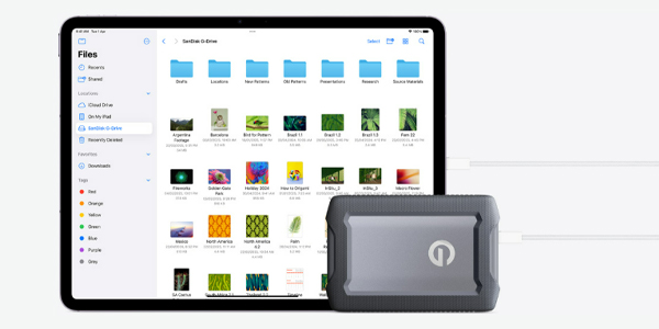 Tablet screen showing a Files app with blue folders and thumbnails, with a rugged external drive connected in front, indicating portable storage use.
