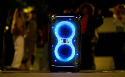 JBL portable Bluetooth speaker glowing with blue LED rings at a nighttime outdoor gathering.