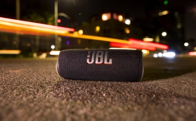 JBL portable Bluetooth speaker lying on asphalt at night with blurred city lights in the background.