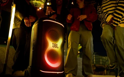 JBL portable speaker with red, yellow, and orange LED lights, surrounded by people at night event. (informative)