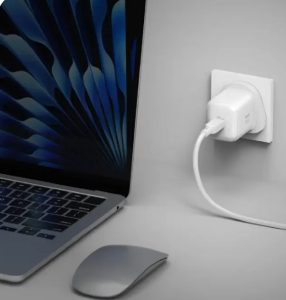 Laptop connected to a wall outlet for charging, with a wireless mouse on the desk nearby.