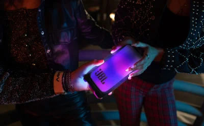 Two people hold a glowing purple JBL speaker in a dimly lit party setting.