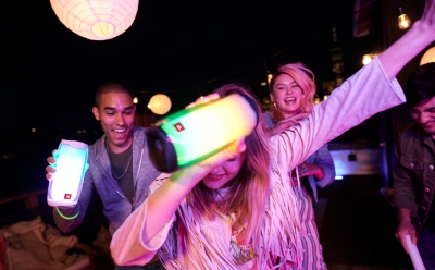 Group of friends dancing at night, holding bright LED glow sticks and lanterns with colorful neon lighting.