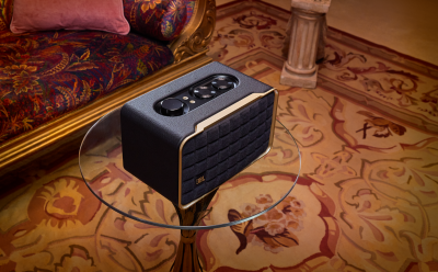 Black JBL portable speaker on a round glass table in a richly patterned living room with ornate upholstered sofa and patterned carpet.”] }Oops. Ensure proper quotes and multiple options. Let's fix.