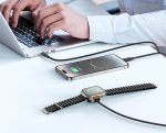 Person typing on a laptop with a smartphone charging on the desk and a smartwatch connected via magnetic charging band nearby.